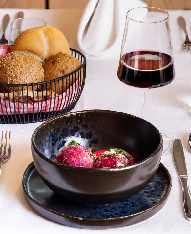 Rote-Bete-Canederli in einer Gourmet-Schale, serviert mit verschiedenen Brotsorten und einem Rotweinglas auf dem Restauranttisch