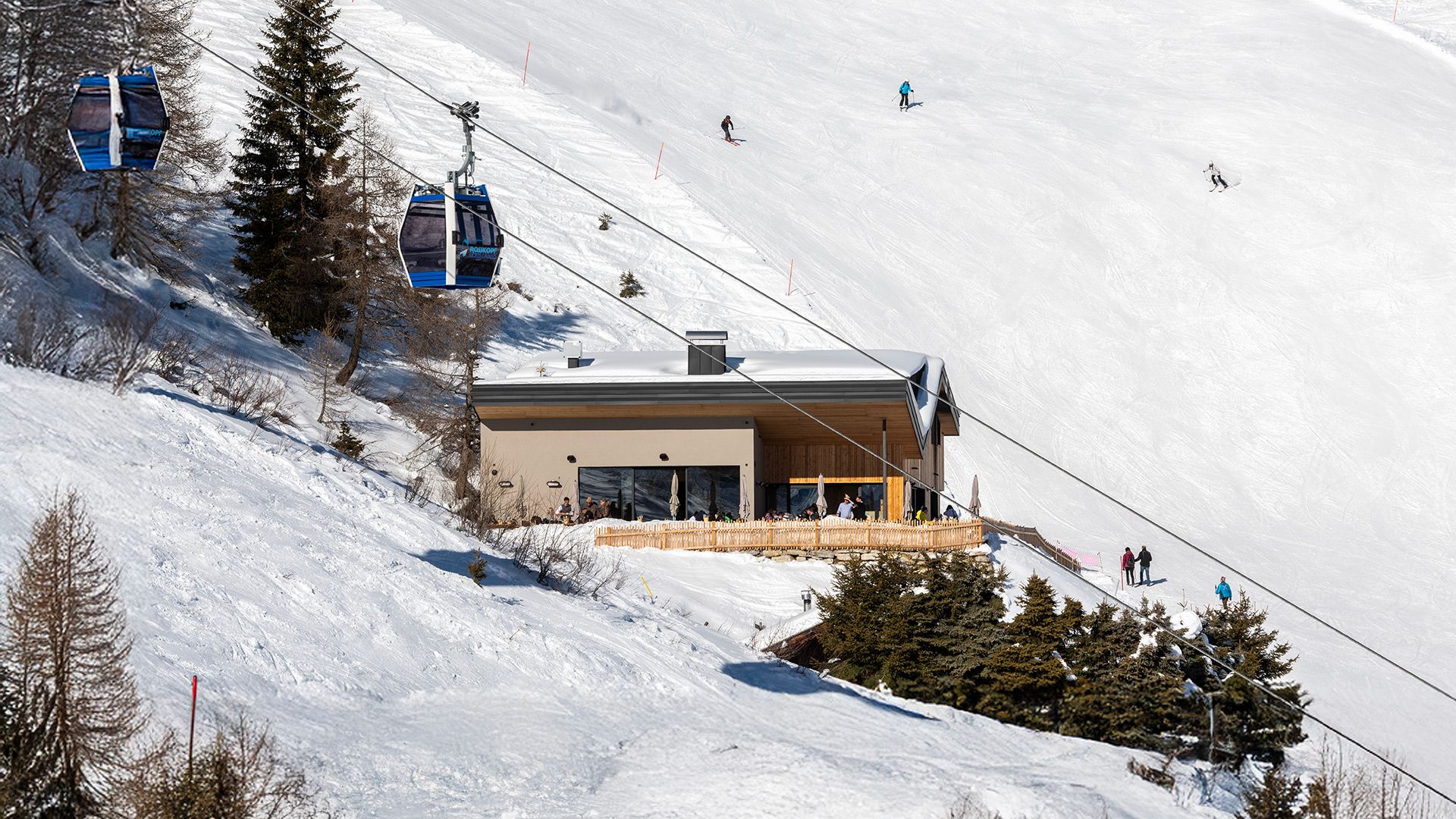 Alpin Chalet Rosskopf mit Panoramaterrasse neben der Seilbahn Monte Cavallo, umgeben von Skipisten mit Skifahrern oberhalb von Vipiteno